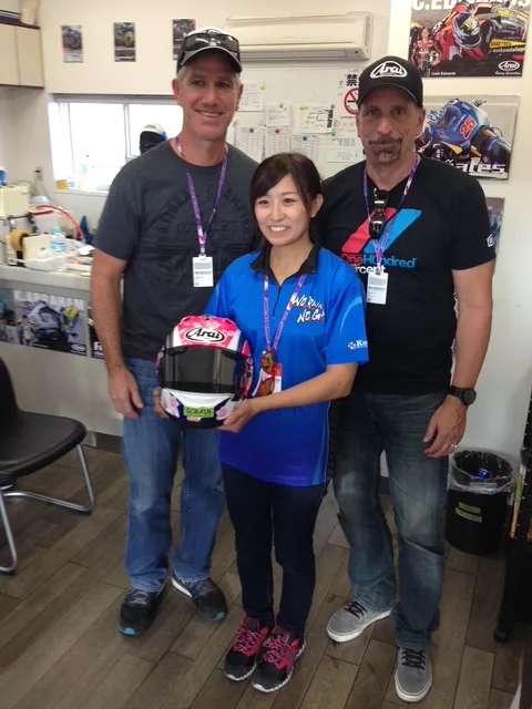 Three people at a race event holding a signed helmet